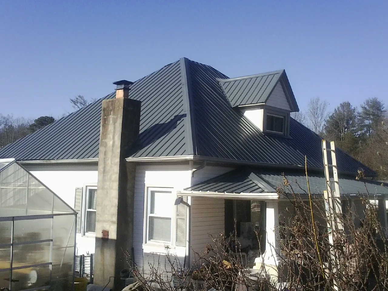 Dark blue standing seam metal roof on a white farmhouse with dormer — Slate & Tile Roof Repair by Roofing Brothers in Bluewater