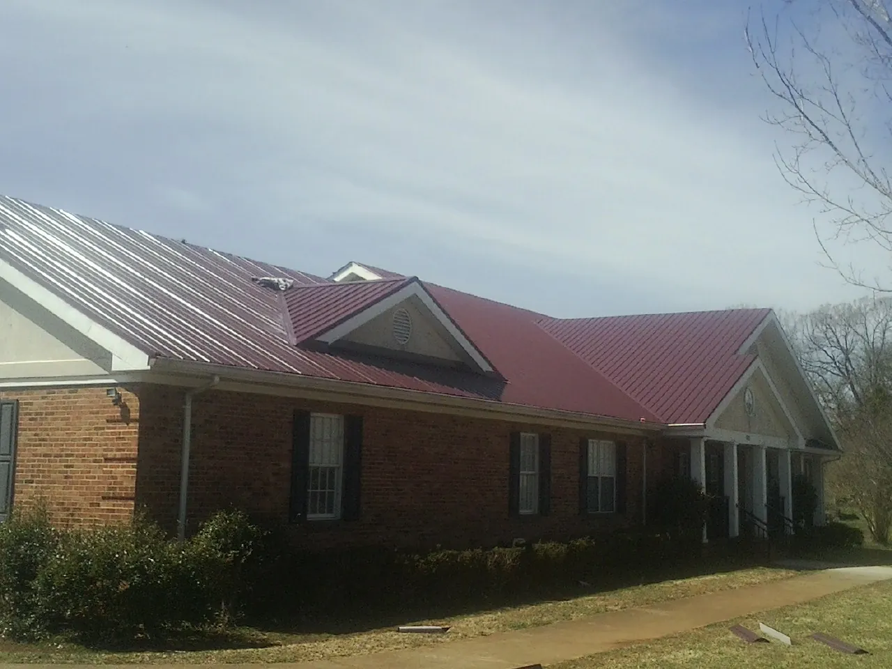 Red metal roof with gabled entries on a long brick building, from a Hail Damage Roof Repair job in Bluewater