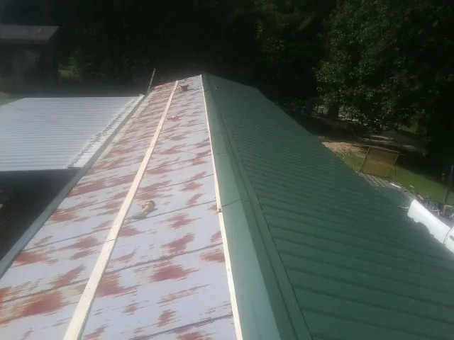 Old rusted panels beside newly installed green metal roofing — Wind Damage Roof Repair by Roofing Brothers in Bluewater