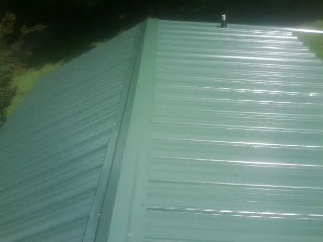 New green metal panels meeting at the ridge of a roof — Flat Roof Repair work by our crew in Bluewater