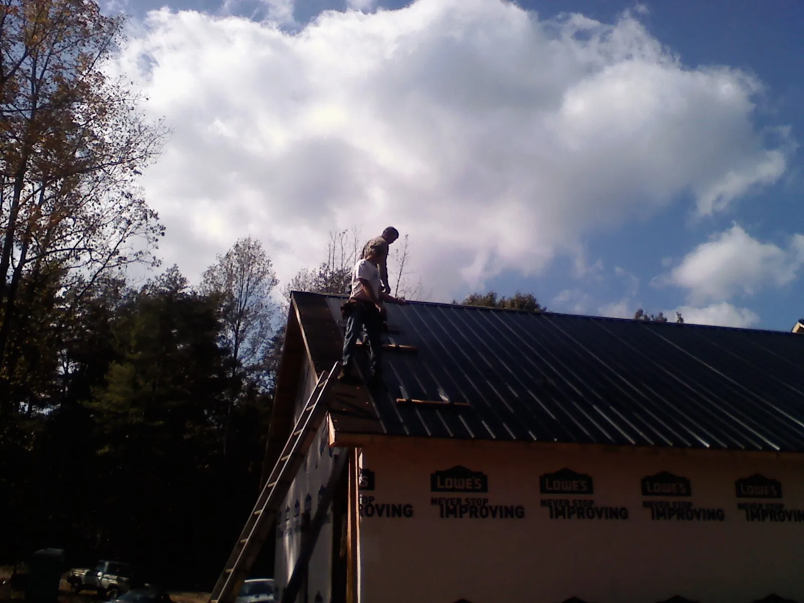Roofer fastening dark metal panels high against a cloudy sky, from a Roof Inspection job in Bluewater