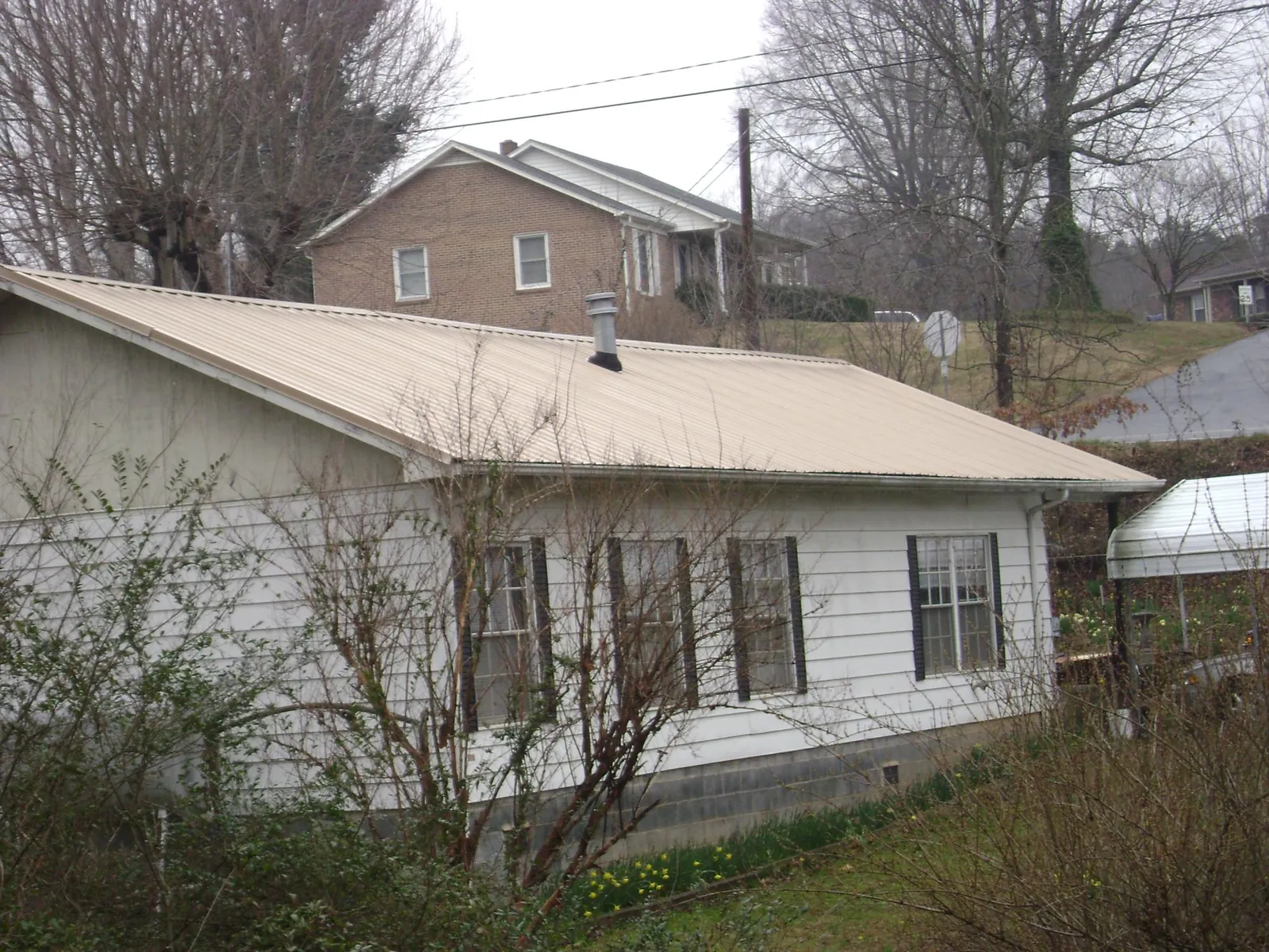Tan metal roof on a white sided house set into a hillside — Commercial Roofing by Roofing Brothers in Bluewater
