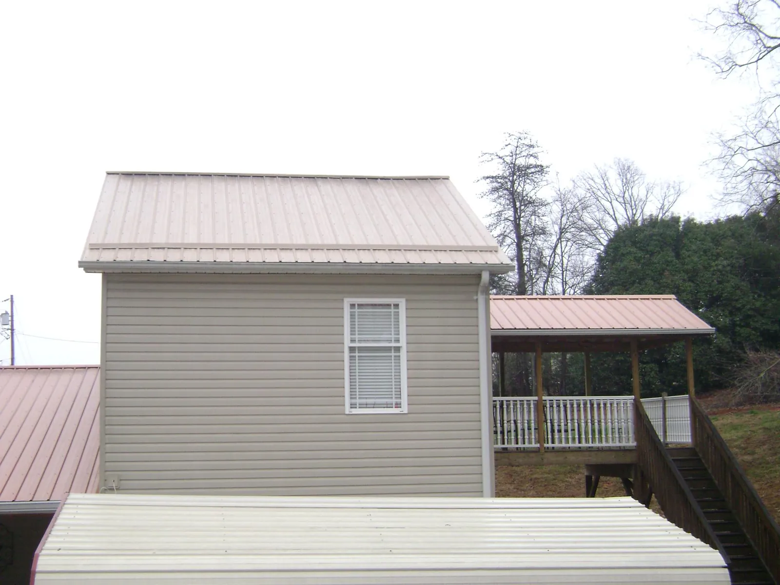 Tan metal roofs on a two story addition and attached porch, from a Roof Replacement job in Bluewater