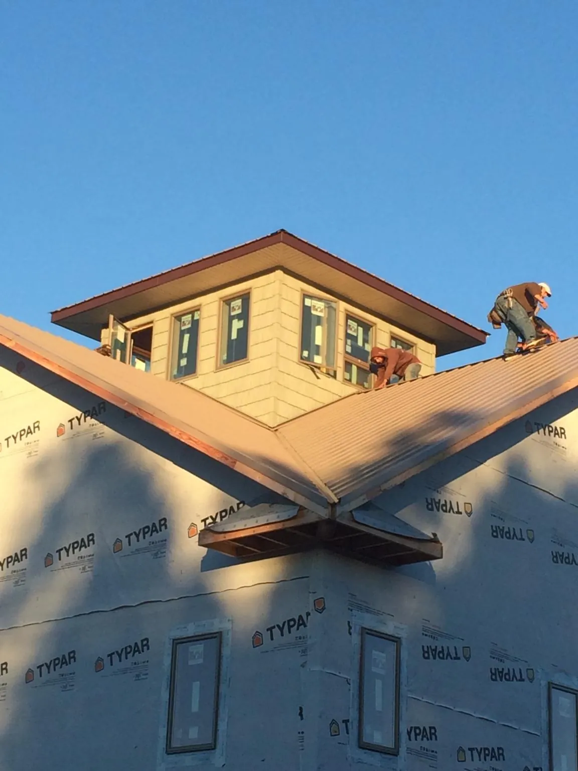Roofers working around a rooftop cupola on a new metal roof at sunset — Roof Waterproofing in Bluewater by Roofing Brothers